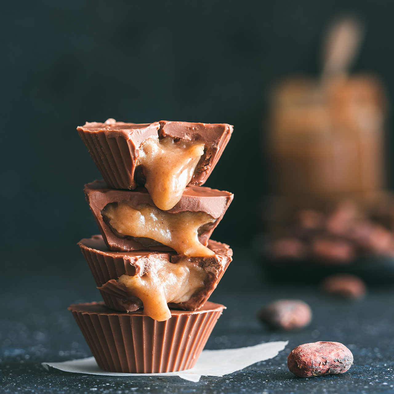 Stack of vegan chocolate cups with caramel on dark tabletop. Homemade vegetarian chocolate caramel cups with raw cacao chocolate. Ideas and recipes for healthy sweets and dessert.