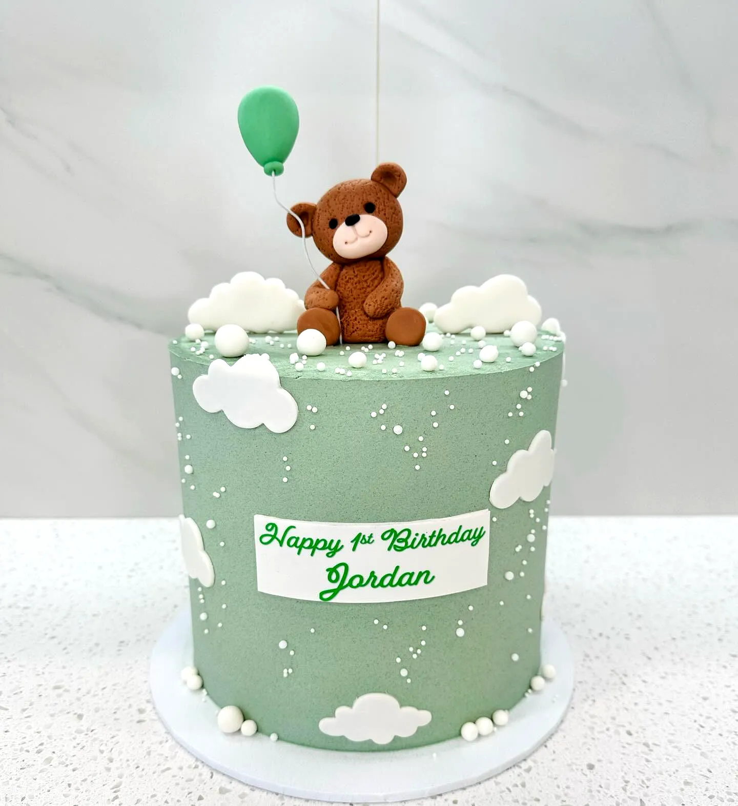 Adorable green birthday cake with playful teddy bear and cloud decorations