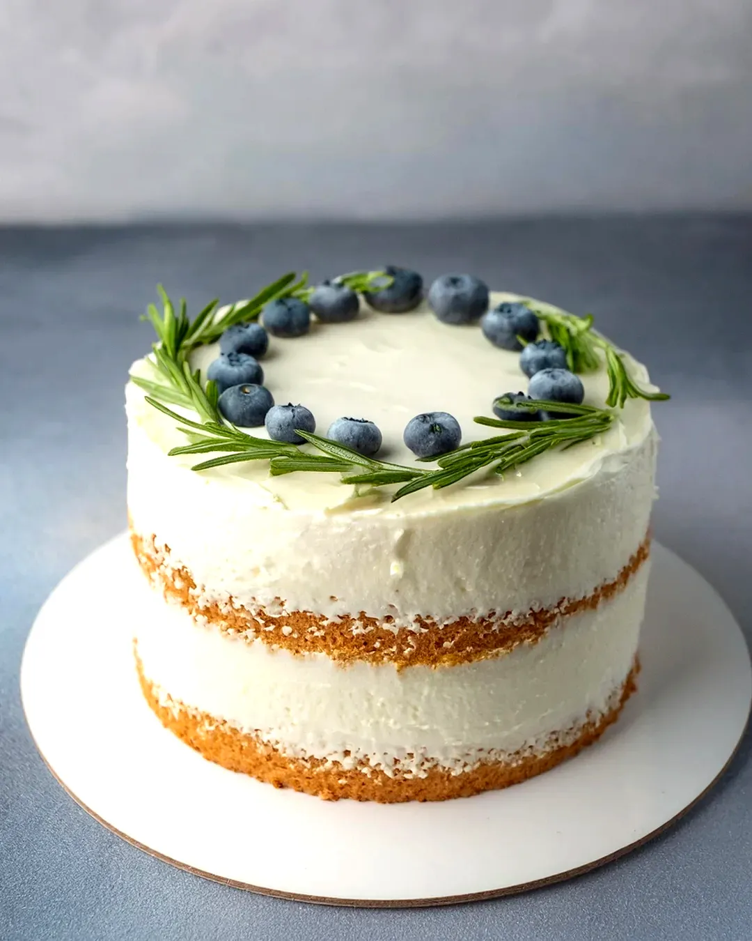 Cute naked white birthday cake with fresh blueberries and rosemary