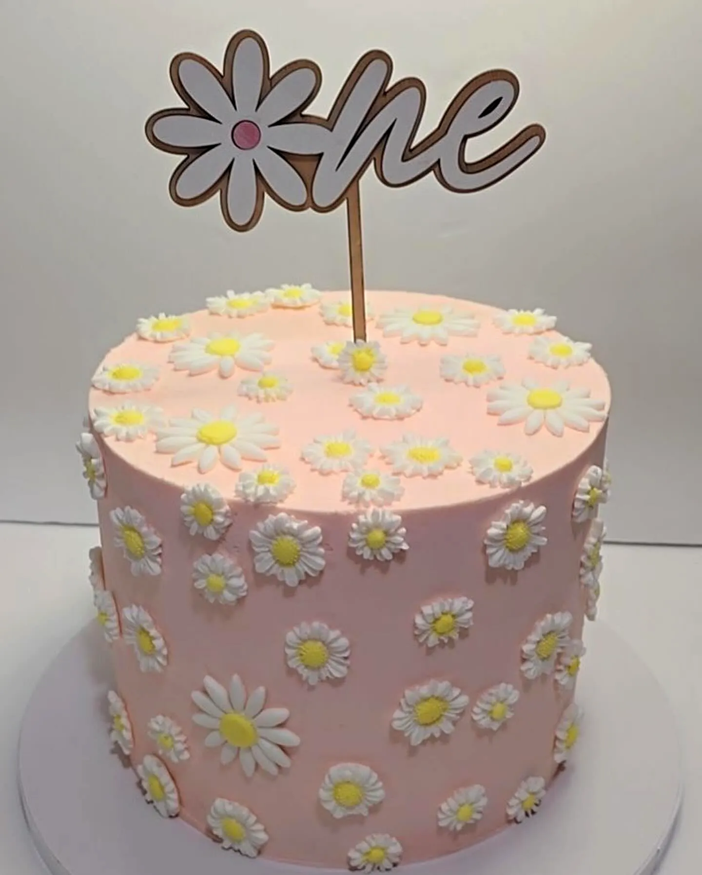 Cute pink 1st birthday cake design with fondant daisies and a one topper