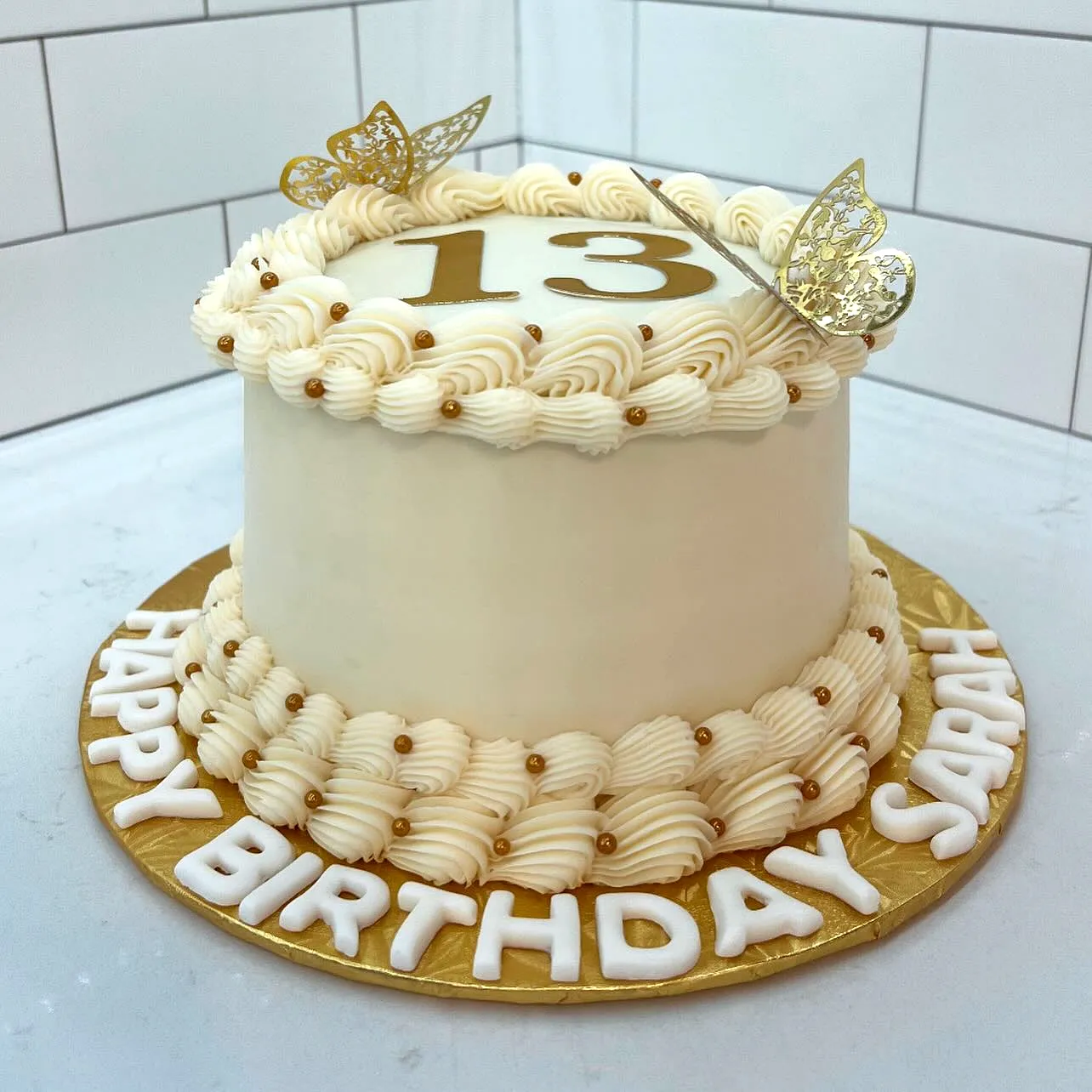 Cute two-tiered 13th birthday cake with golden accents and butterflies