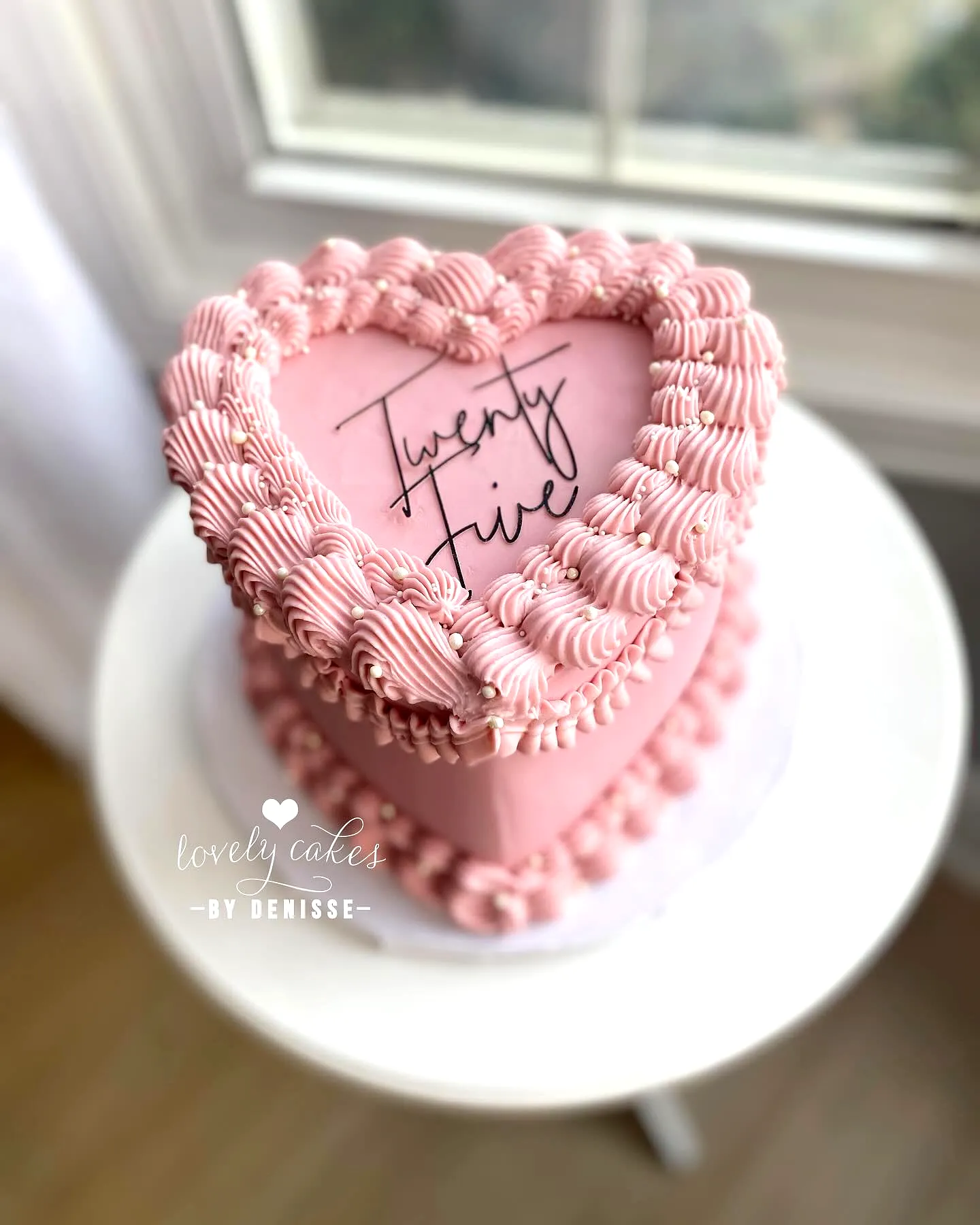 Cute two-tiered heart-shaped 25th birthday cake in soft pink with elegant swirls