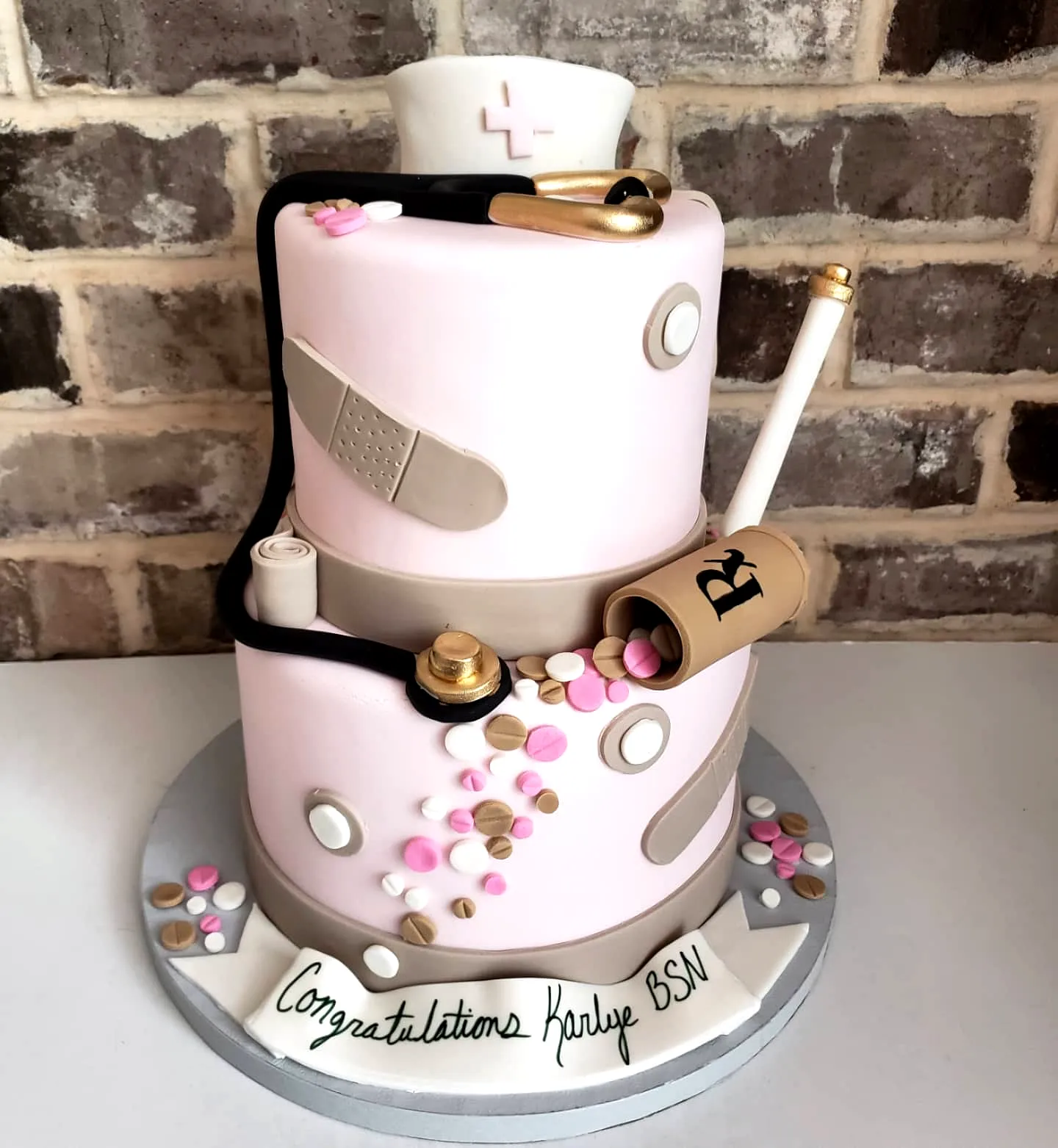 Cute two-tiered nurse graduation cake in pink and white with fun decorations