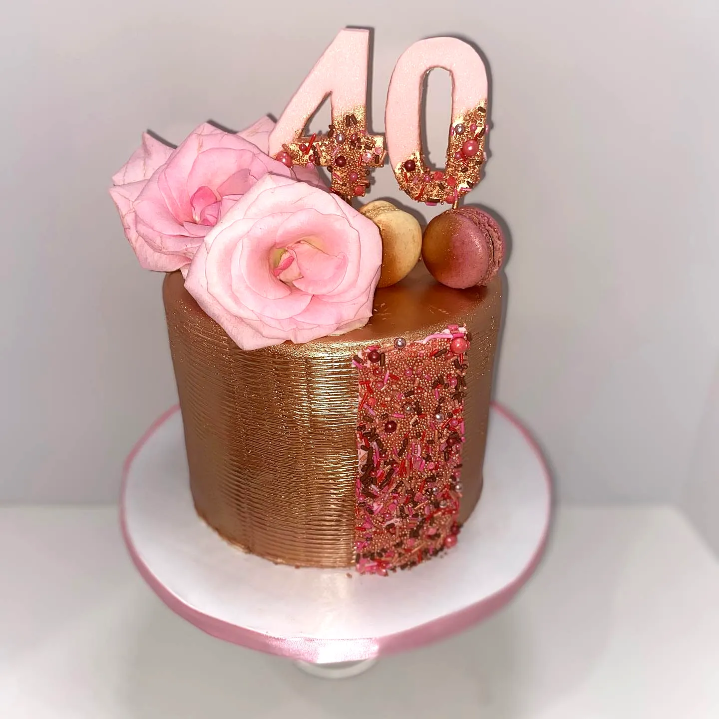 Elegant rose gold birthday cake design with fresh flowers and macarons