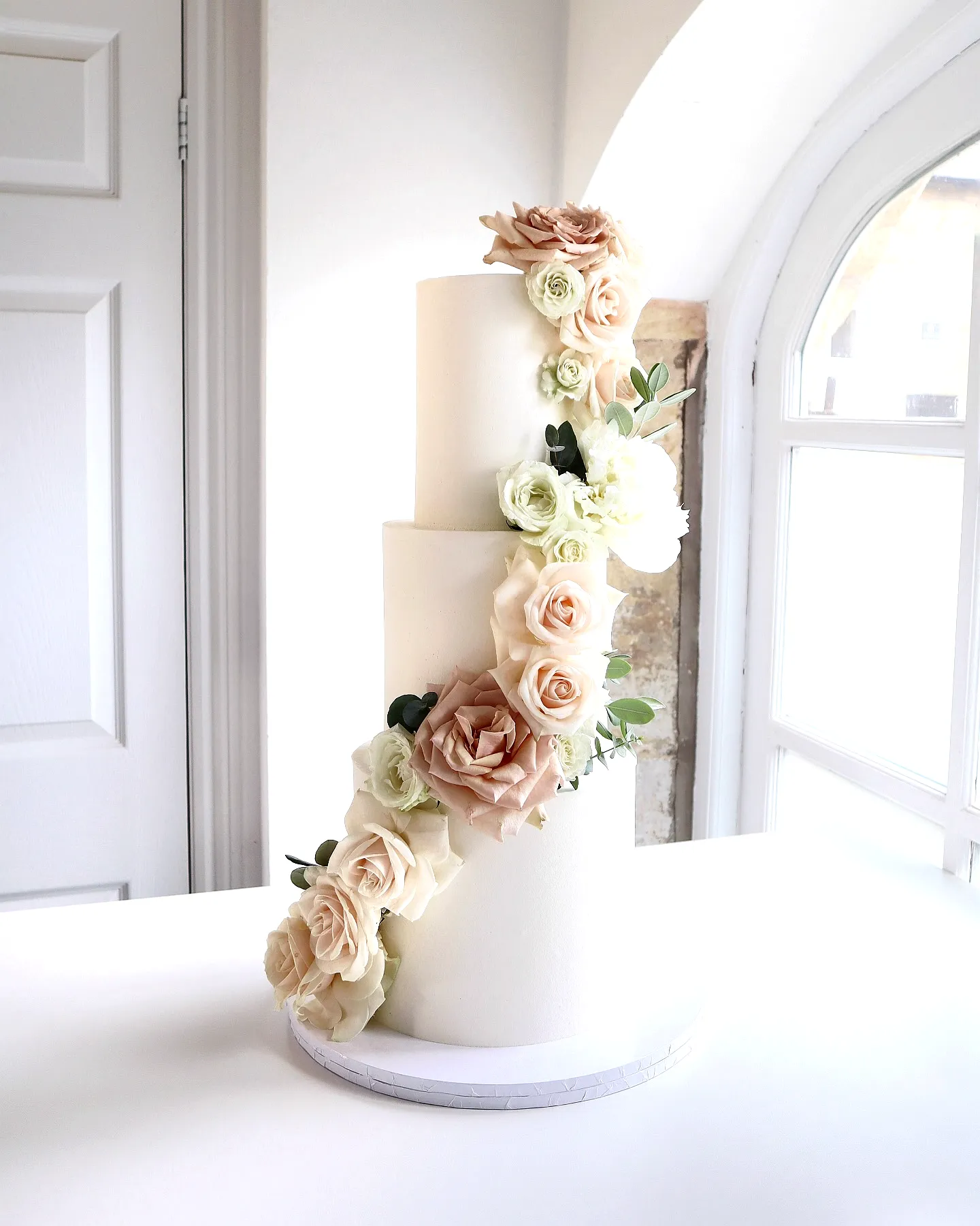 Elegant three tier wedding cake design with blush roses and greenery