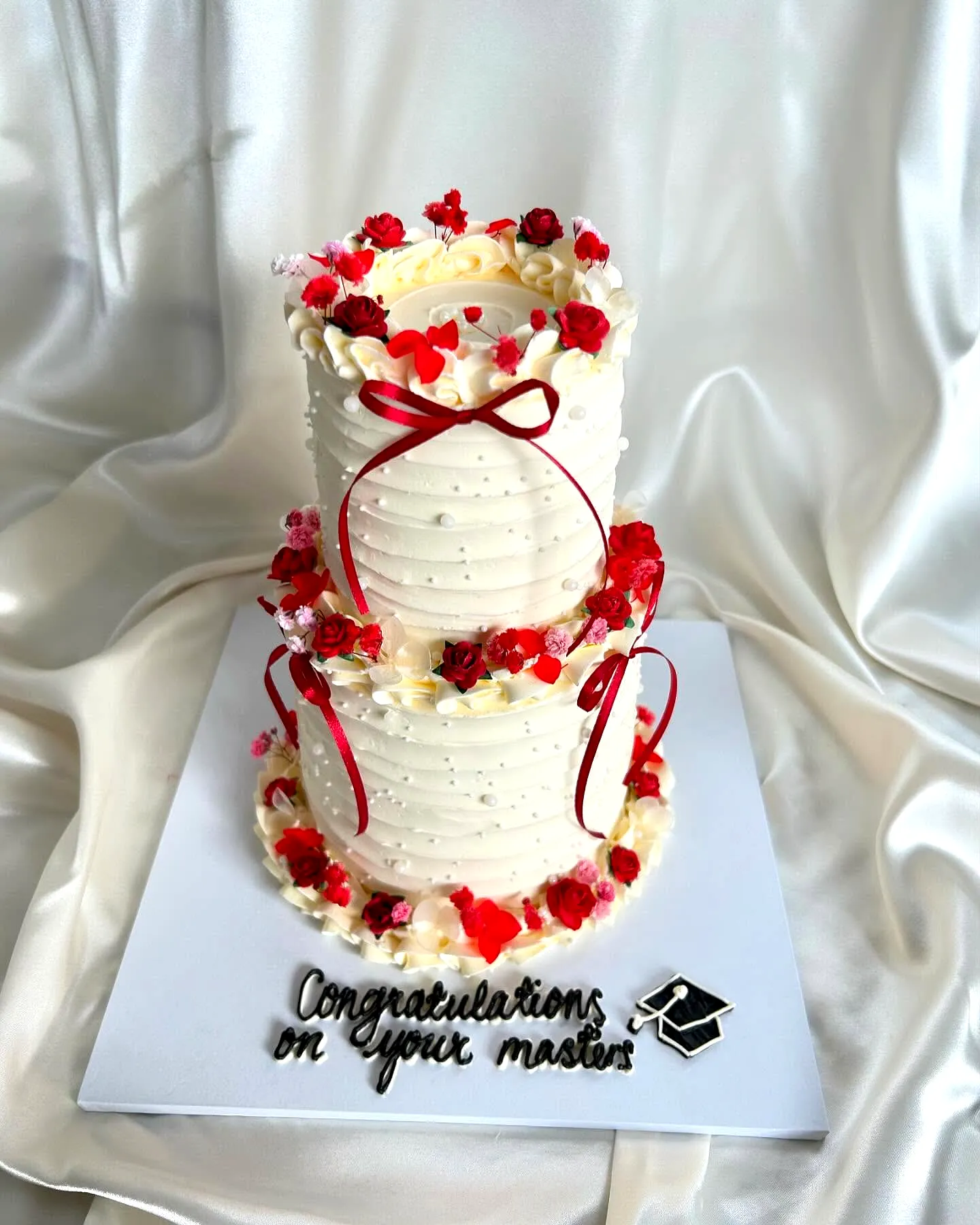 Elegant two tier graduation cake with red roses and smooth buttercream frosting