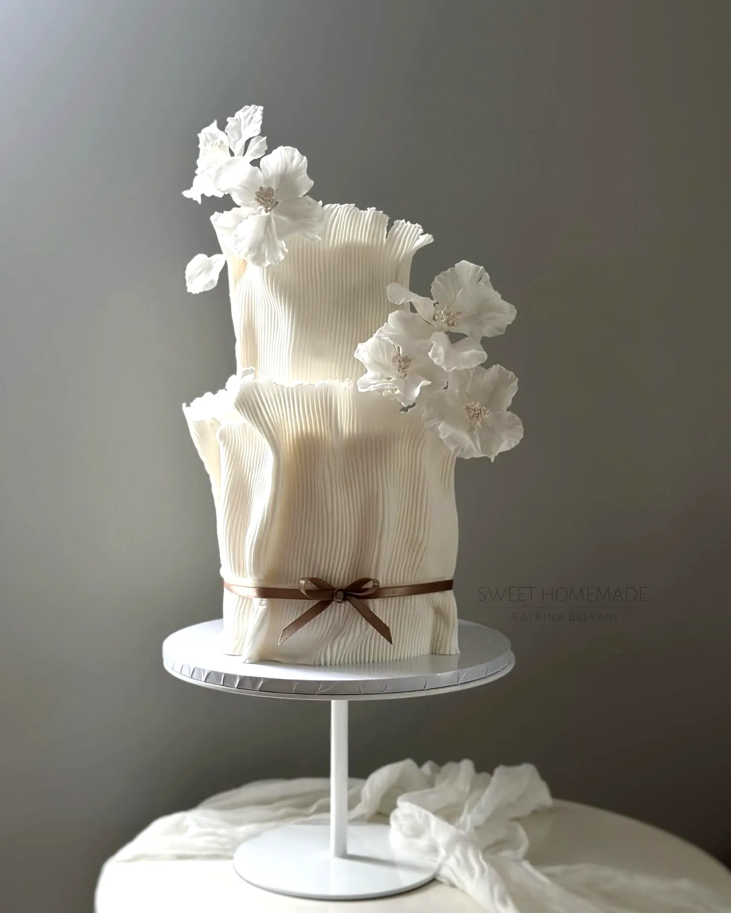 Elegant two-tiered wedding cake design with pleated texture and flowers