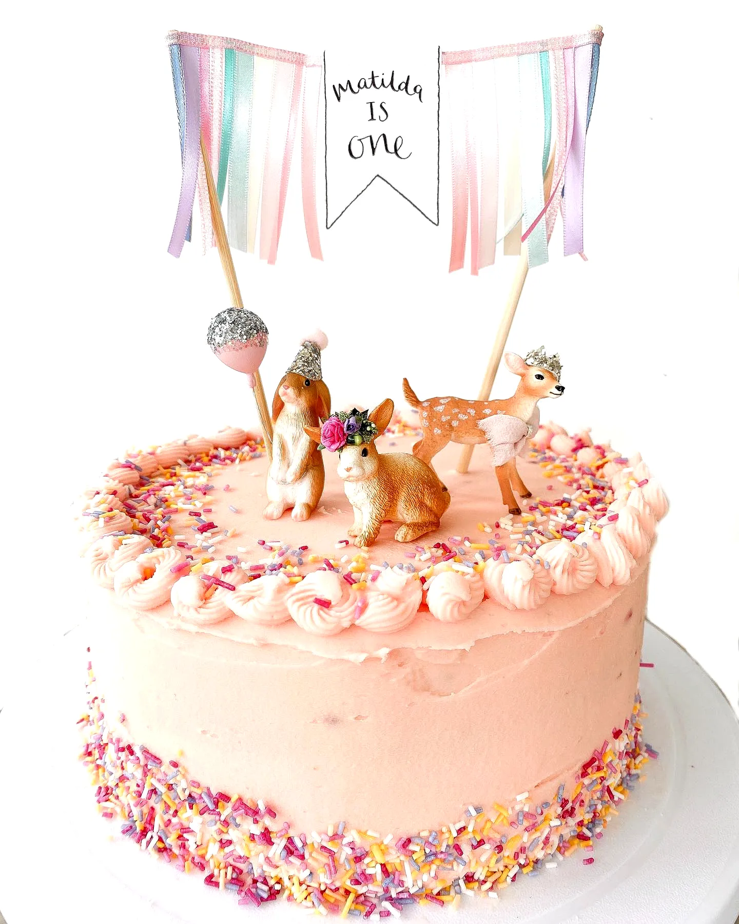 Whimsical 1st Birthday Cake Design with Pink Buttercream and Animal Decor